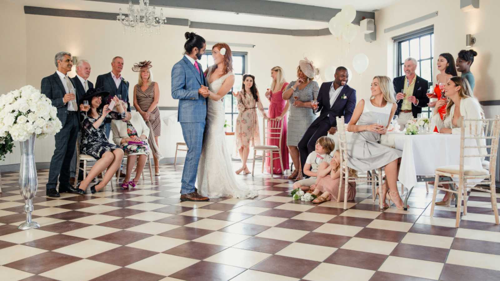 Beautiful couple are sharing their first dance on their wedding day. All of their guests are sitting around the dancefloor watching them.