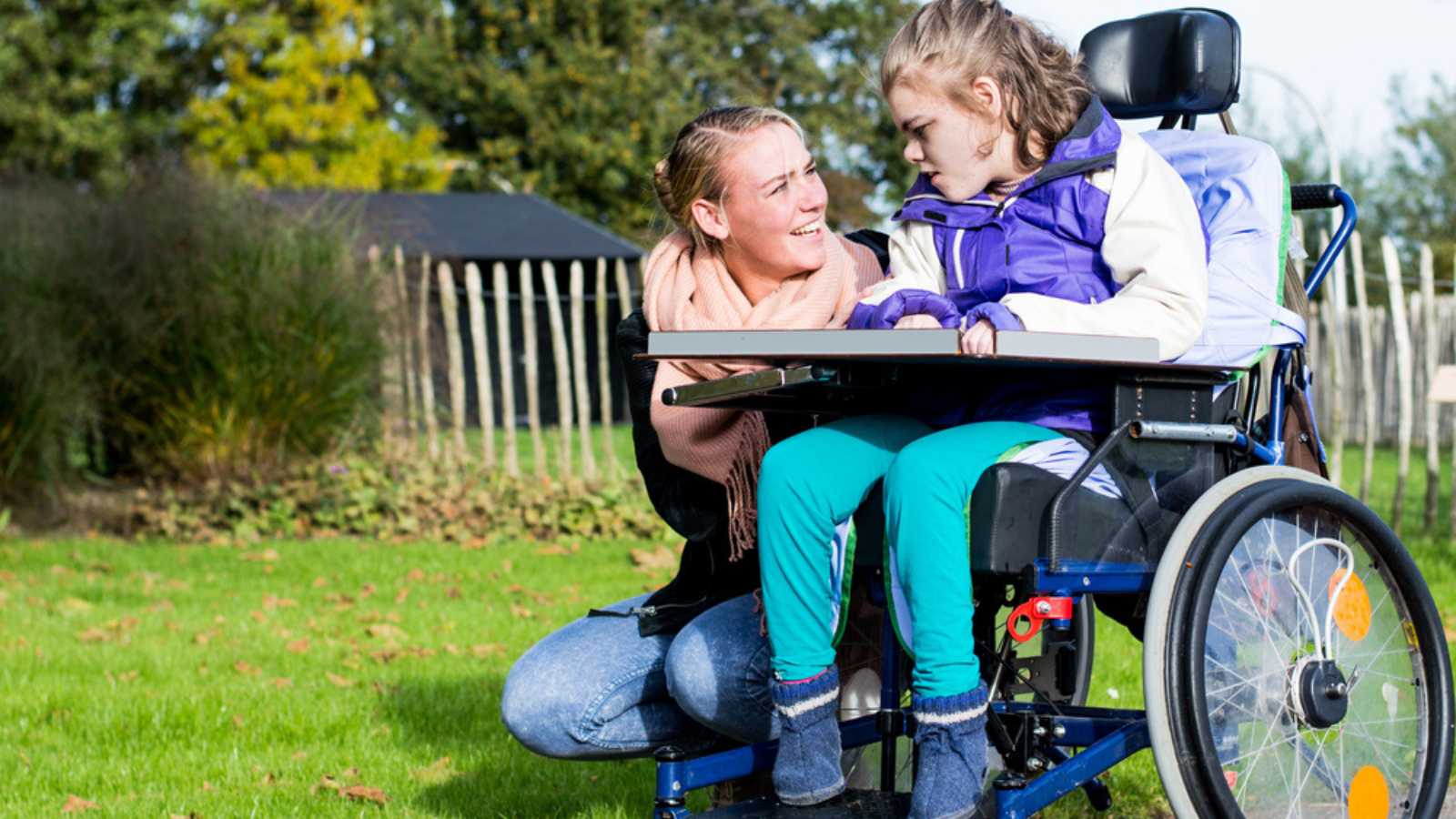 Disabled child in a wheelchair relaxing outside with a care assistant / Working with disability