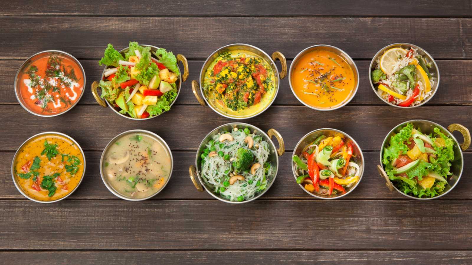 Vegan or vegetarian restaurant dishes top view, hot spicy indian soups, rice and salads in copper bowls. Traditional indian cuisine meal assortment on wood background. Healthy eastern local food