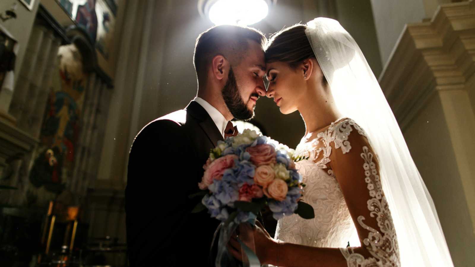 Daylight makes a halo around dreamy wedding couple standing in church