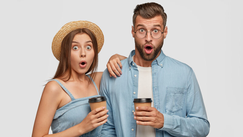 Stupefied lovely couple notice something terrible, have shocked expressions, drink aromatic coffee after work. Attractive European girl leans at shoulder of boyfriend, hear bad unexpected news