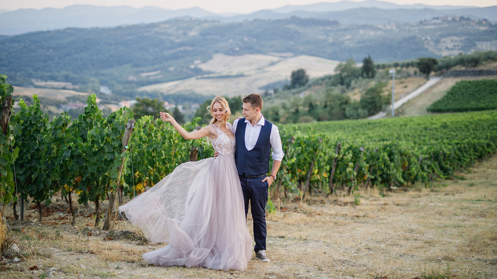 young beautiful wedding couple walking at sunset in Tuscany in Italy near the vineyards bride in beautiful dress groom stylishly dressed