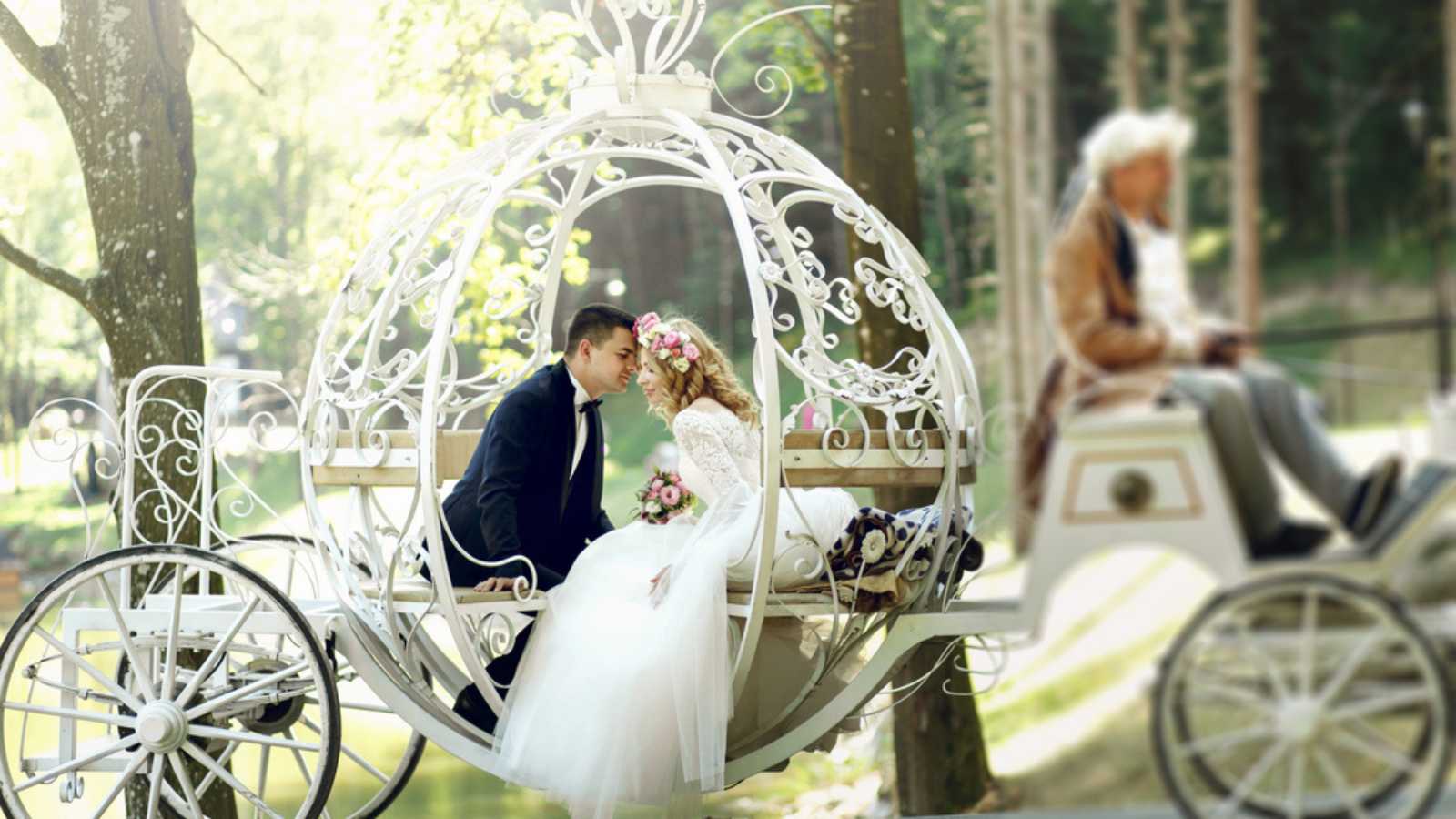 Handsome groom kissing blonde beautiful bride in magical fairy tale carriage in sunlit park