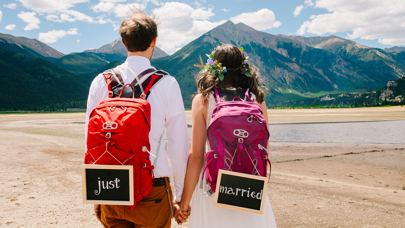 Newlyweds. Groom and bride with backpacks and just married signs are facing the mountains. Adventure of the married couple concept. Starting a new journey together idea.