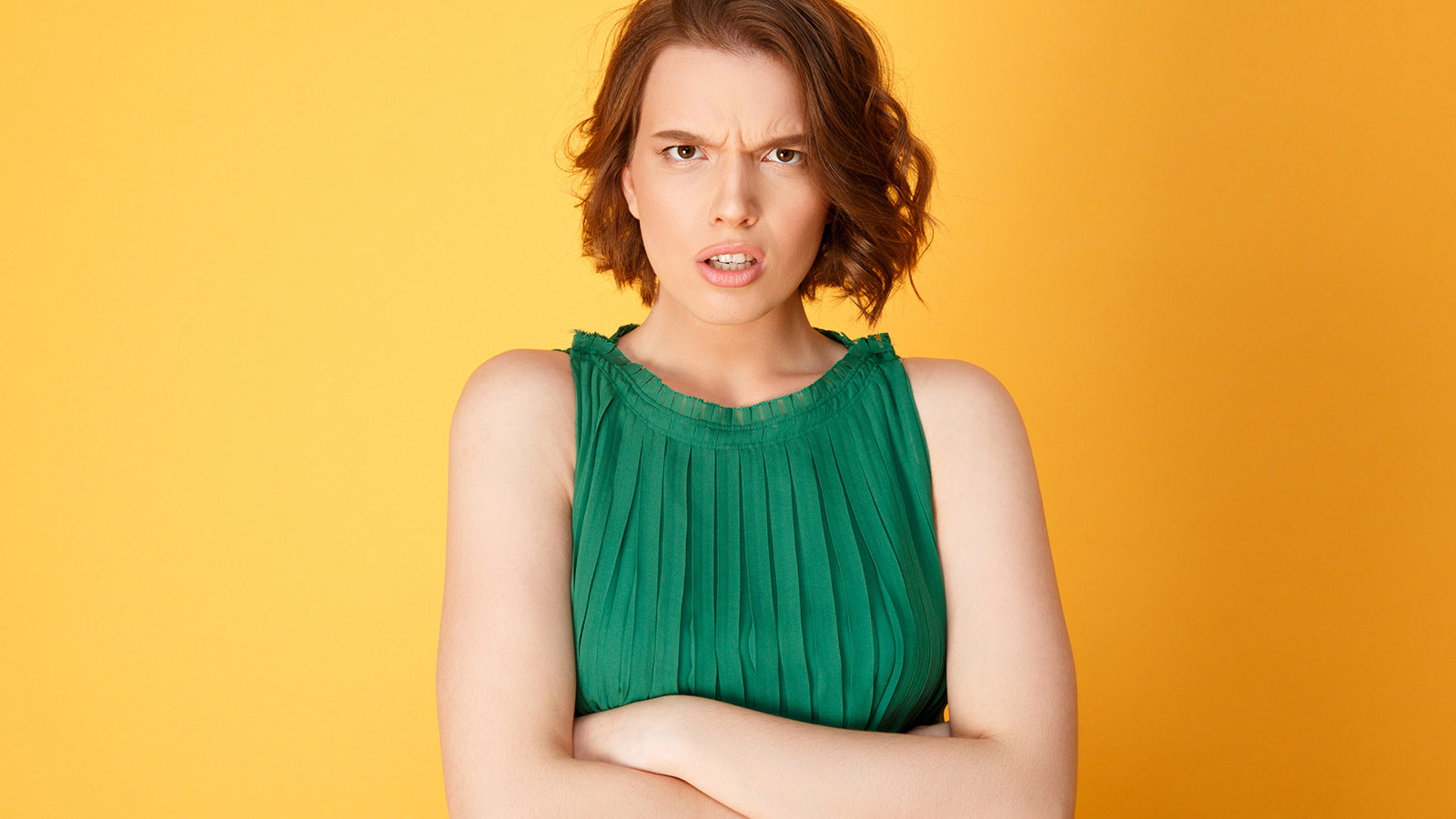 portrait of angry woman with arms crossed looking at camera isolated on orange