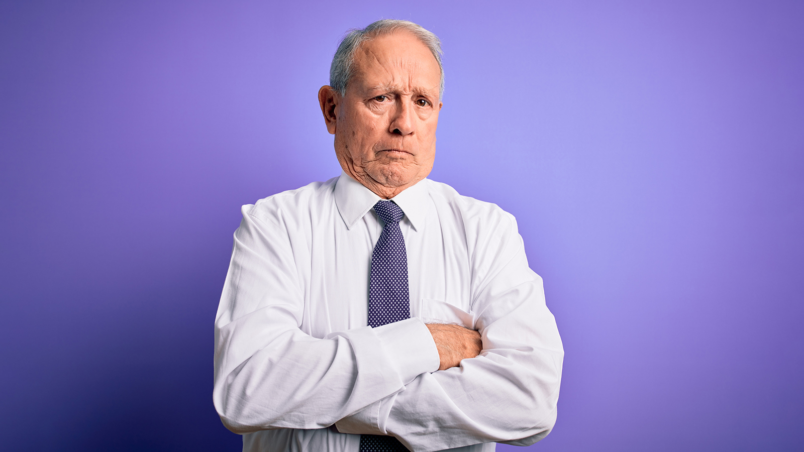 Grey haired senior business elegant man standing over purple isolated background skeptic and nervous, disapproving expression on face with crossed arms. Negative person.