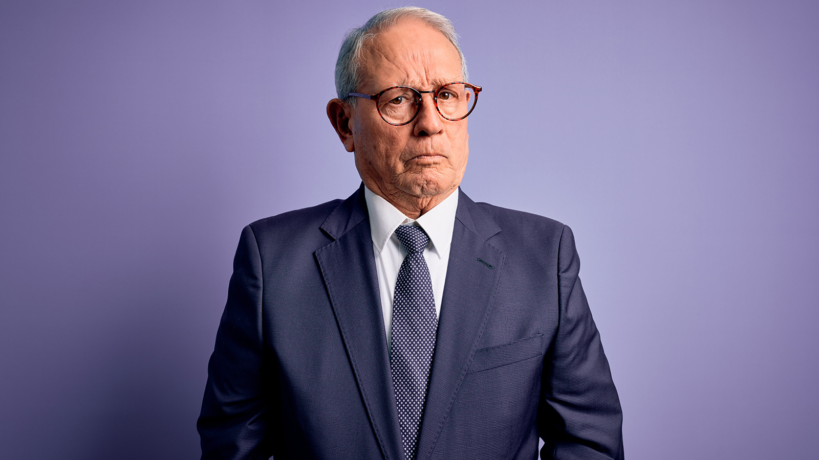 Grey haired senior business man wearing glasses and elegant suit and tie over purple background depressed and worry for distress, crying angry and afraid. Sad expression.
