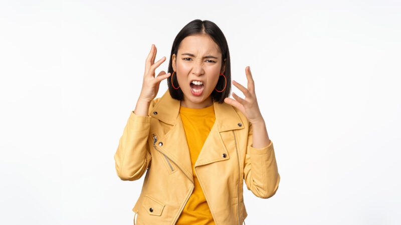 Asian angry woman arguing, shaking hands angry and screaming, shouting with frustrated face, standing over white background.Asian angry woman arguing, shaking hands angry and screaming, shouting with frustrated face, standing over white background.