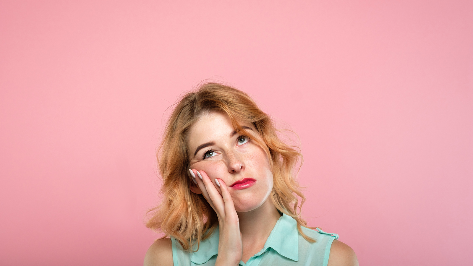 facial expression. low mood and emotion. bored unimpressed disinterested woman looking up. young beautiful blond girl portrait on pink background.