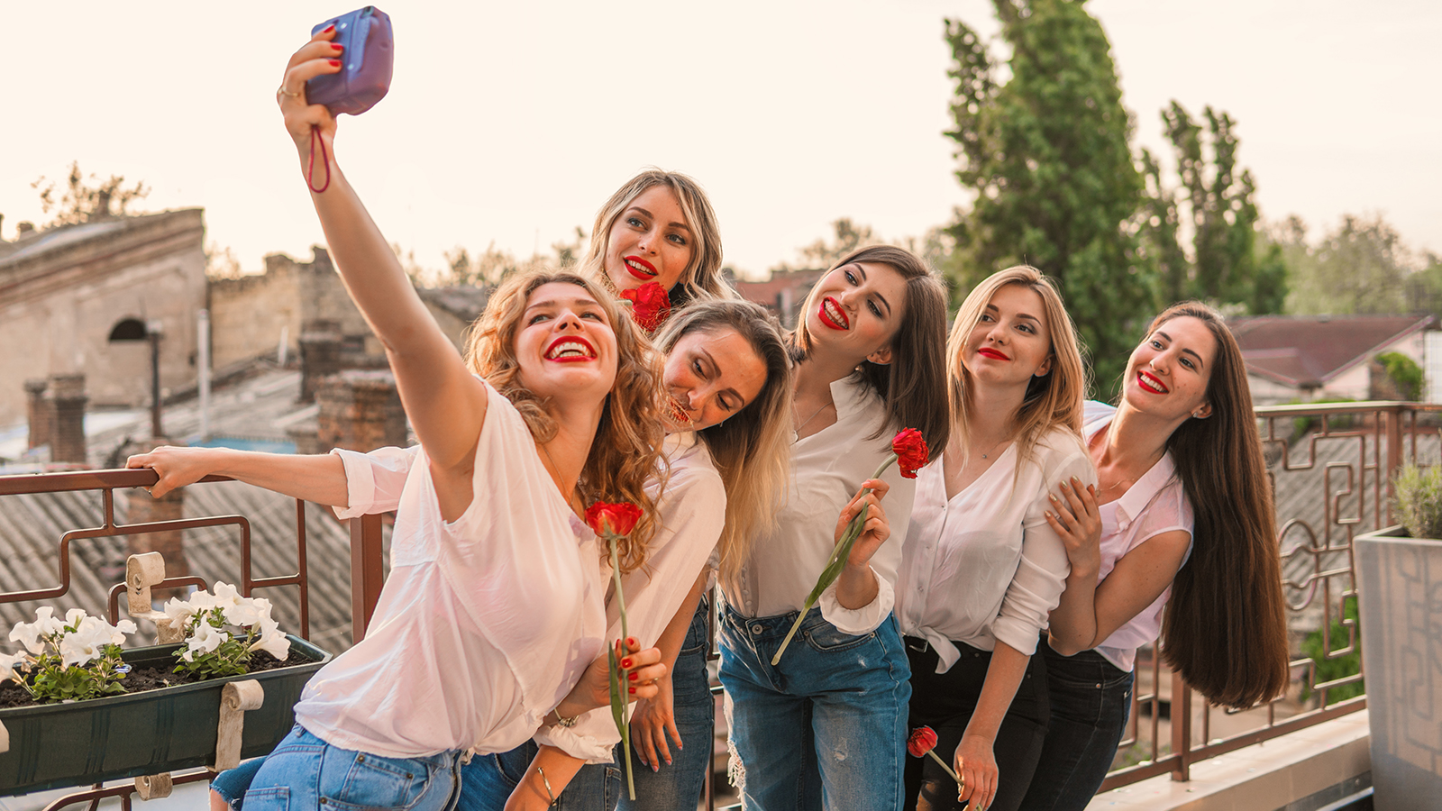 Girls Party. Beautiful Women Friends on the balcony or roof taking selfie with flowers At Bachelorette Party. They wear same clothes