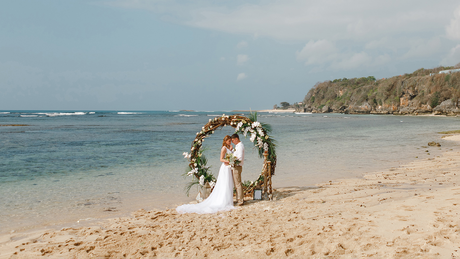 Romantick wedding cople standing on the beach near round wooden arch in boho rustc style after ceremony by the sea. Moment of tenderness and love. Beach wedding Bali