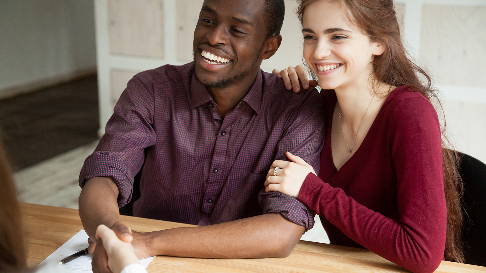 Happy attractive multiracial couple shaking hands with advisor or realtor, smiling african american man handshaking at meeting after signing family mortgage investment contract or loan agreement