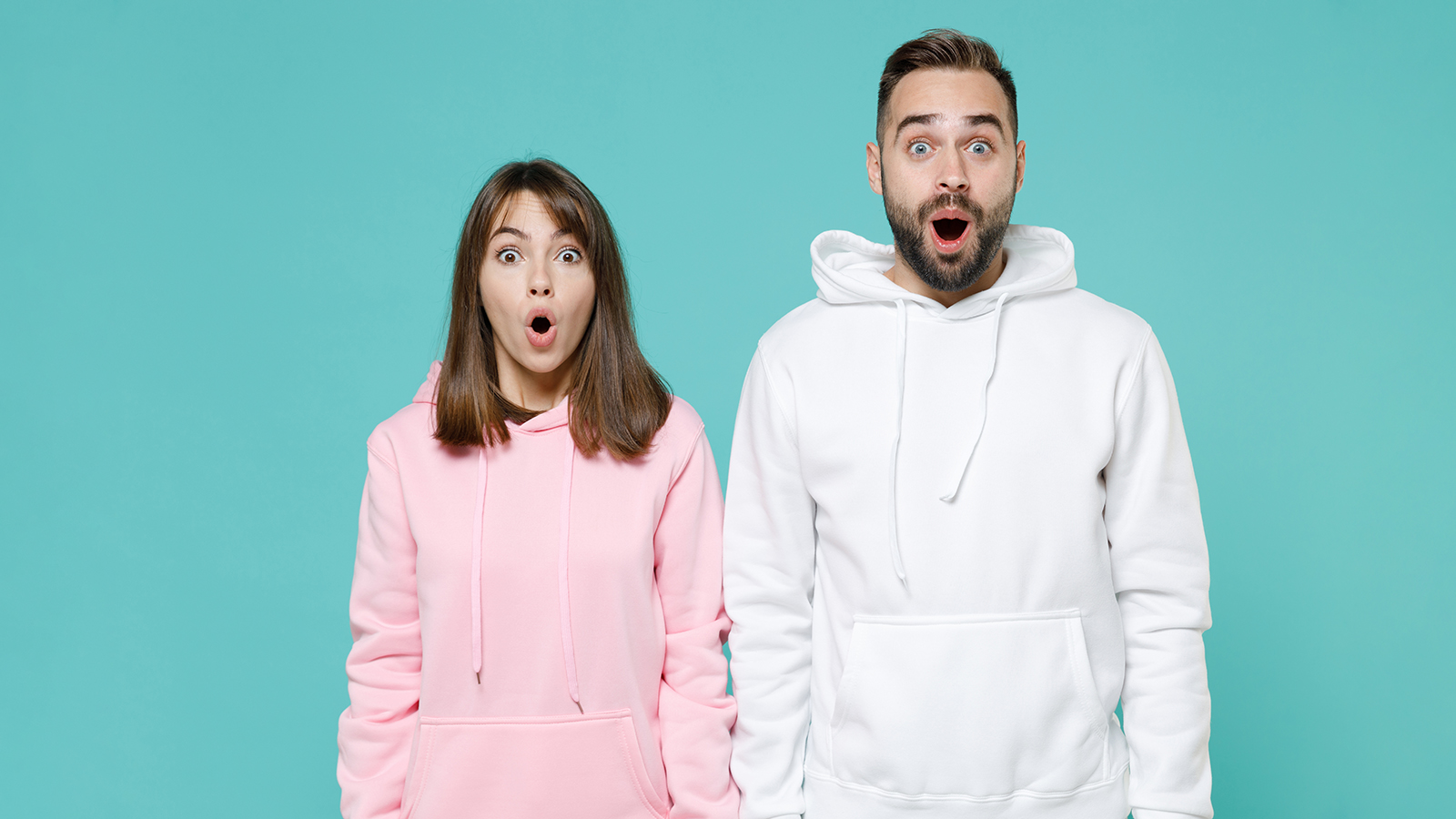 Shocked amazed young couple two friends man woman 20s wearing white pink casual hoodie standing keeping mouth open looking camera isolated on blue turquoise colour wall background studio portrait