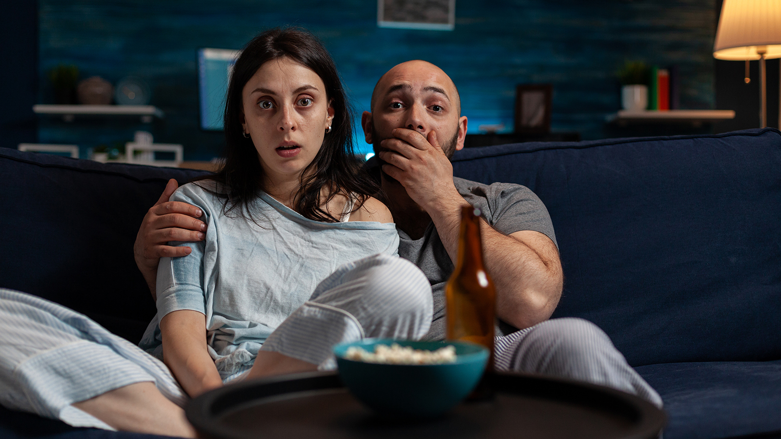 POV of shocked partners watching cinema movie on television, feeling surprised and doing wow expression. Man and woman with mouth open looking at scary film on TV channel program.