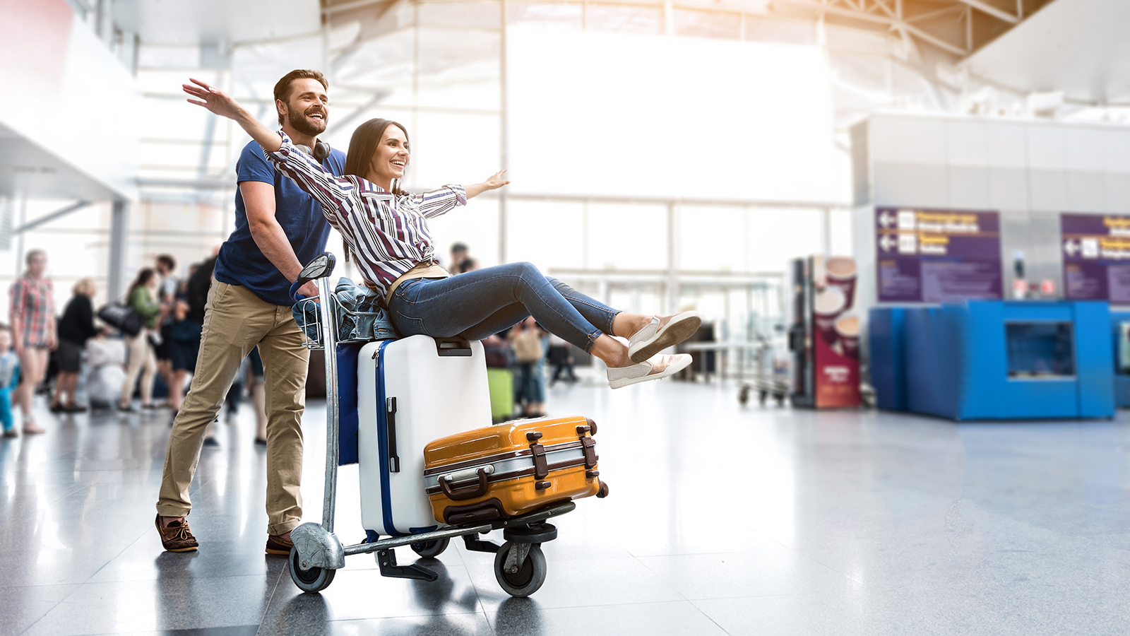 I believe I can fly. Cheerful woman is sitting on baggage and man pulling cart forward. They looking ahead with joyous smile. Copy space on right side