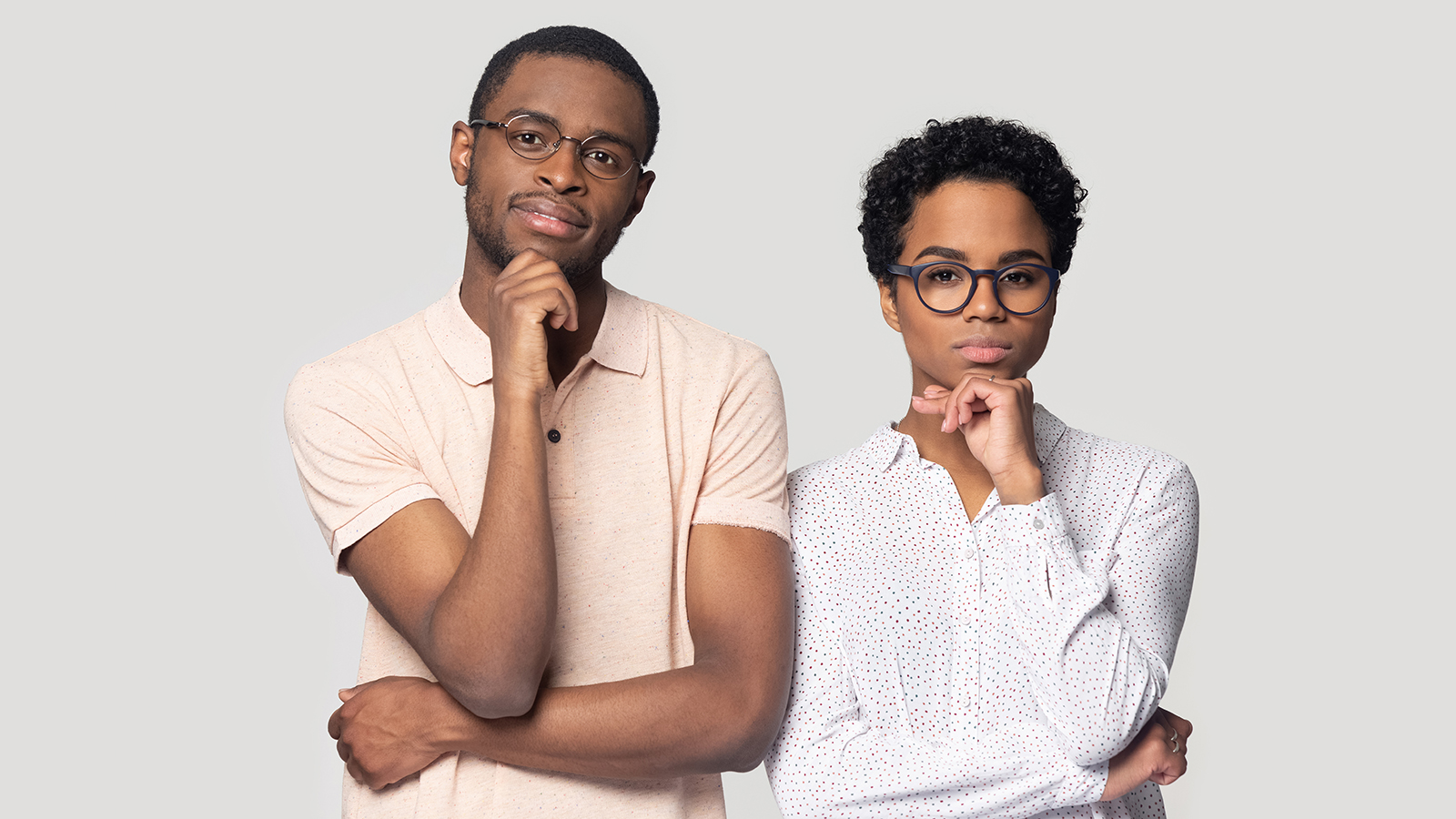 Thoughtful african American couple in glasses stand isolated on grey studio background look at camera making decision, pensive ethnic black millennial man and woman hold hands at chin thinking