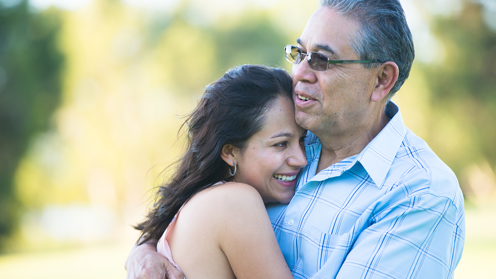 Portrait proud hispanic father cuddling happy relaxed smiling attractive adult daughter outdoor, blurred background.