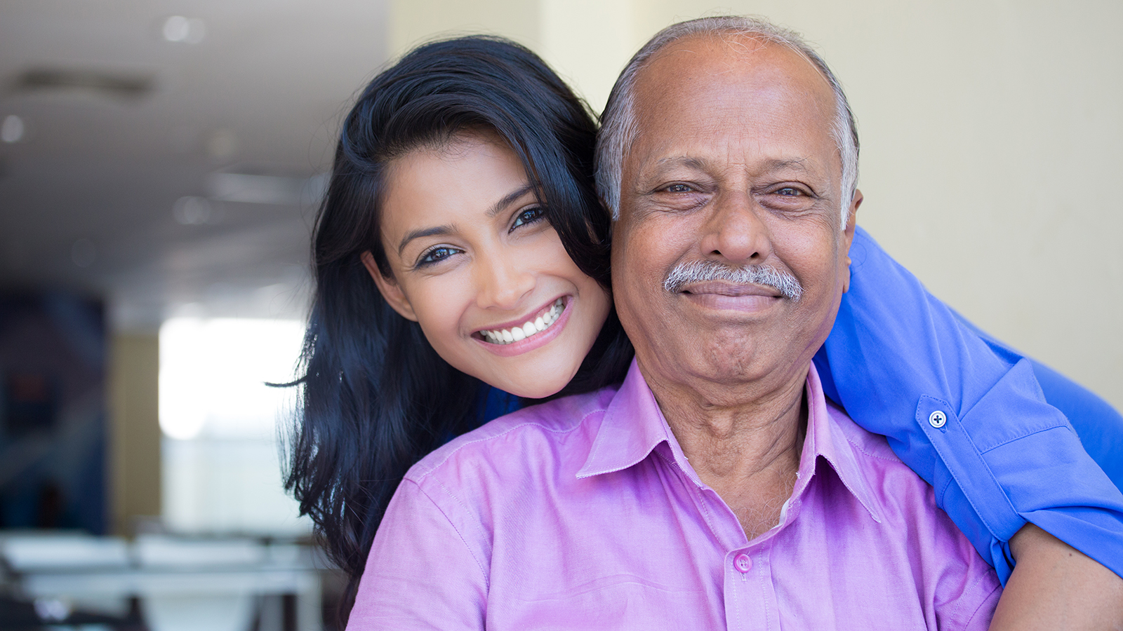 Closeup portrait, family, young woman in blue shirt holding older man in pink collar button down from behind, happy isolated indoors home background