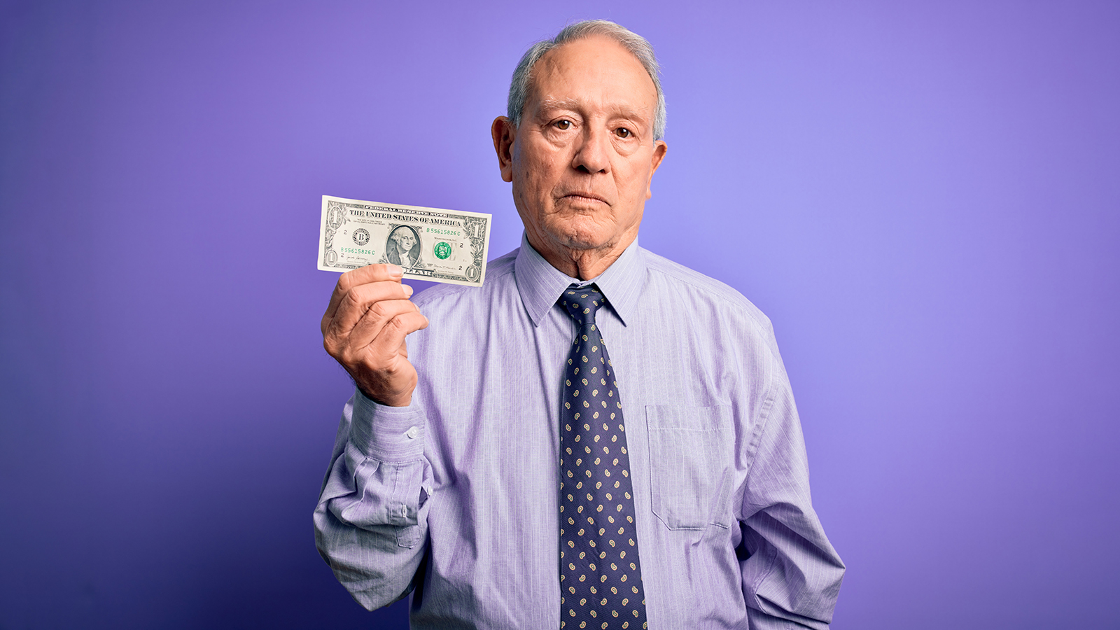Senior grey haired man holding one dollar bank note over purple background with a confident expression on smart face thinking serious