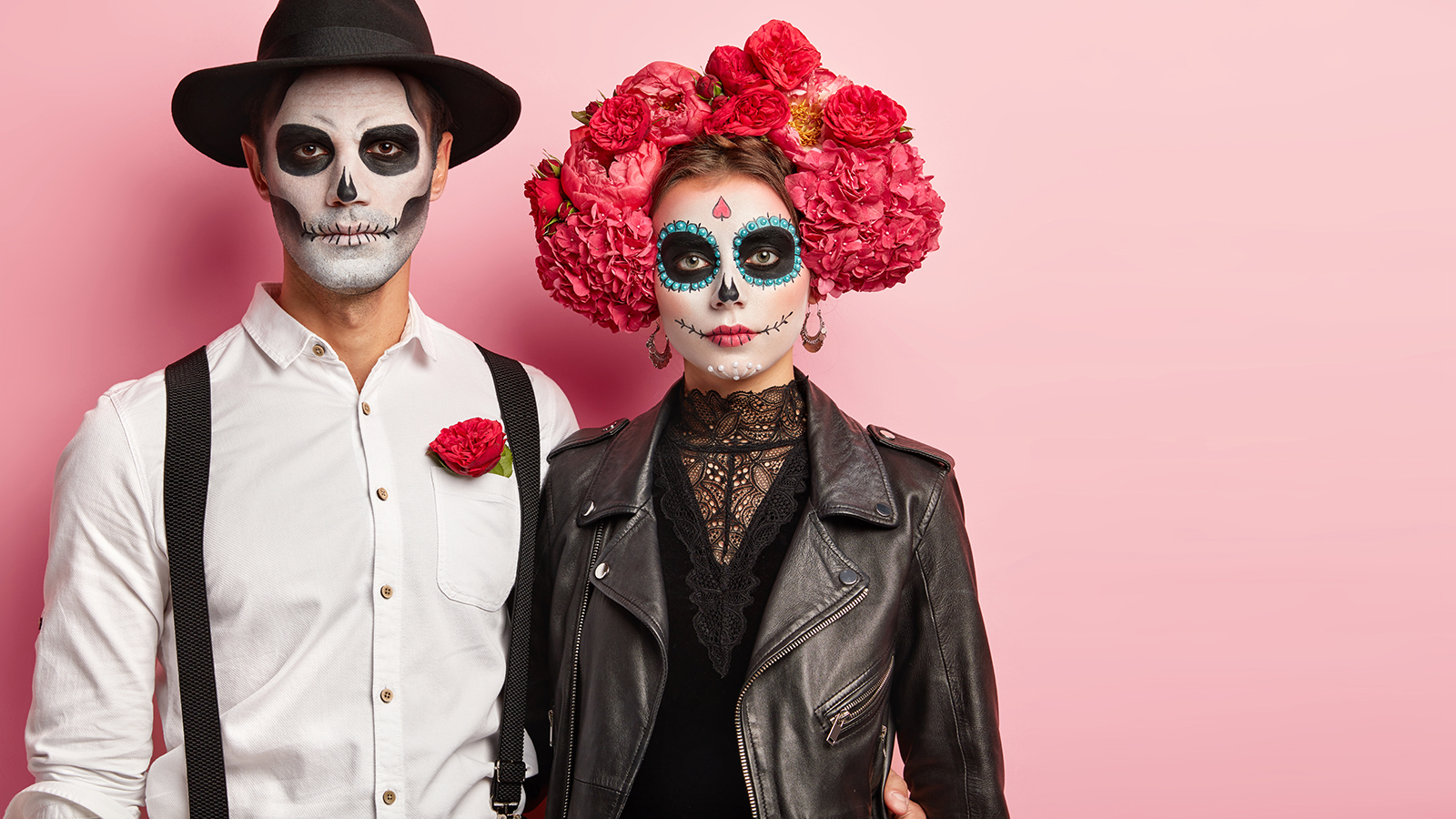 Bridal couple celebrate typical Mexican holiday, wear special costumes, have wedding on cemetery, pose indoor against pink background, blank space aside. Day of Dead carnival and celebration.