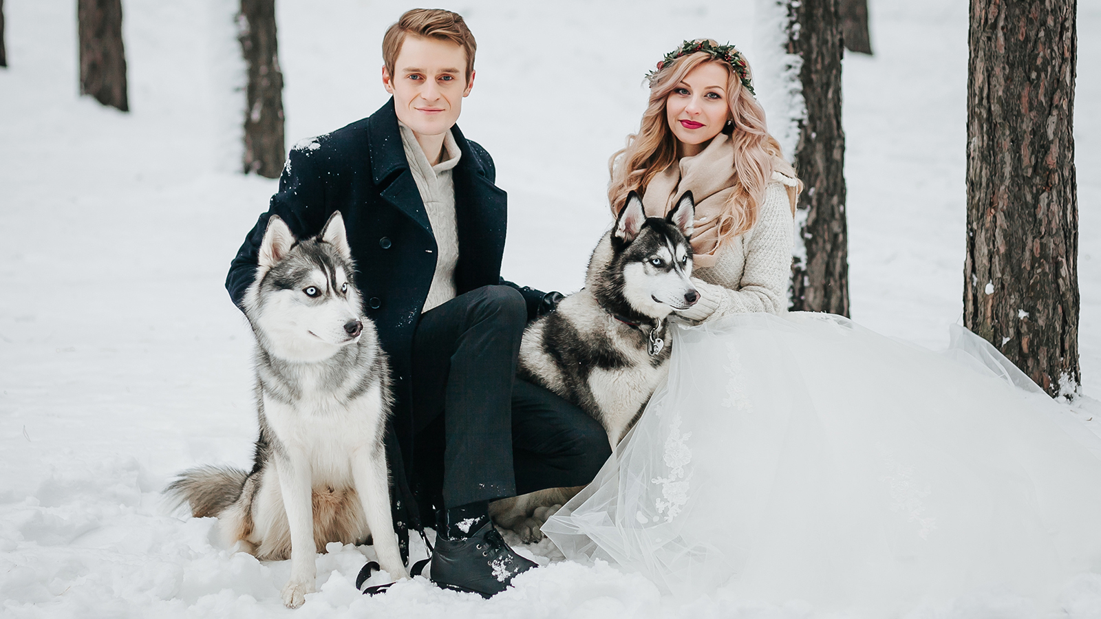 Cheerful couple are playing with siberian husky in snowy forest. Winter wedding