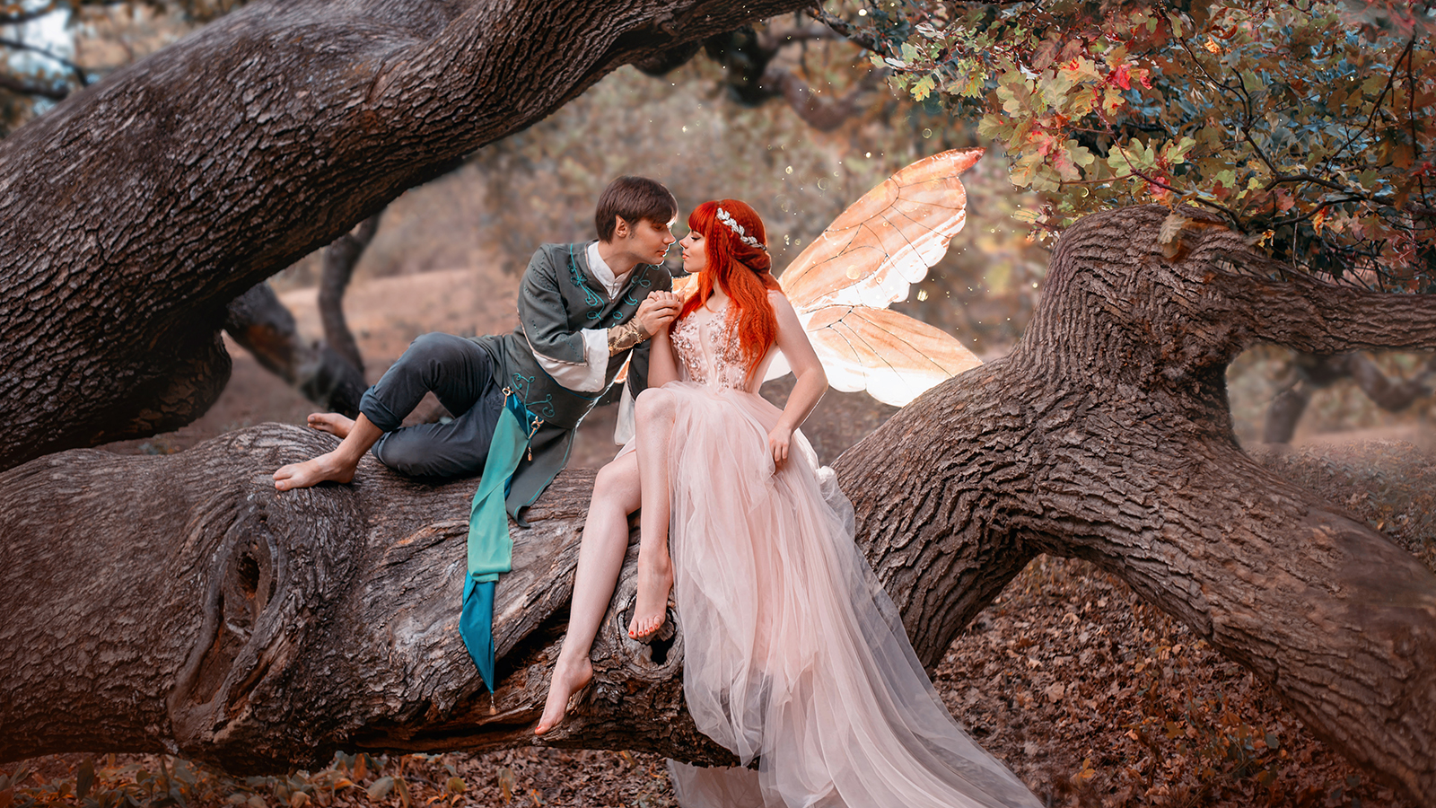 Young couple in love. A man and a woman are hugging on huge tree. Themed creative wedding bright fantasy photography. Fairy woman in long pink dress with bright golden wings. A man in an elf costume