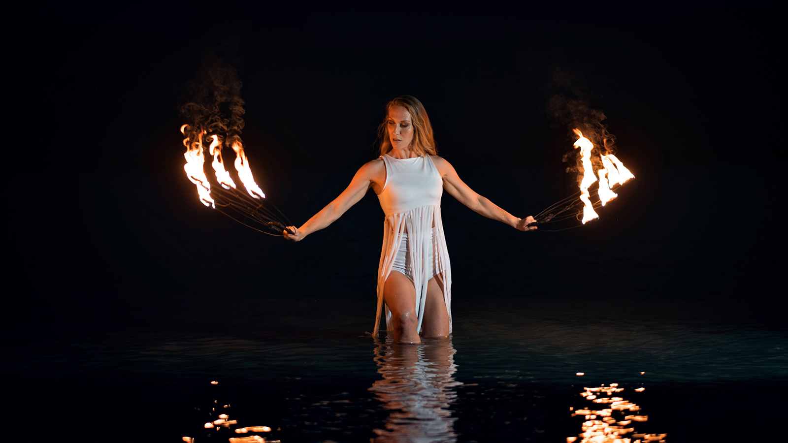 Caucasian woman dancing with fire in the water. Fire show at sea. Acrobatics on the beach. Yoga and relaxation at sunset. Spectacular circus performance. model body.