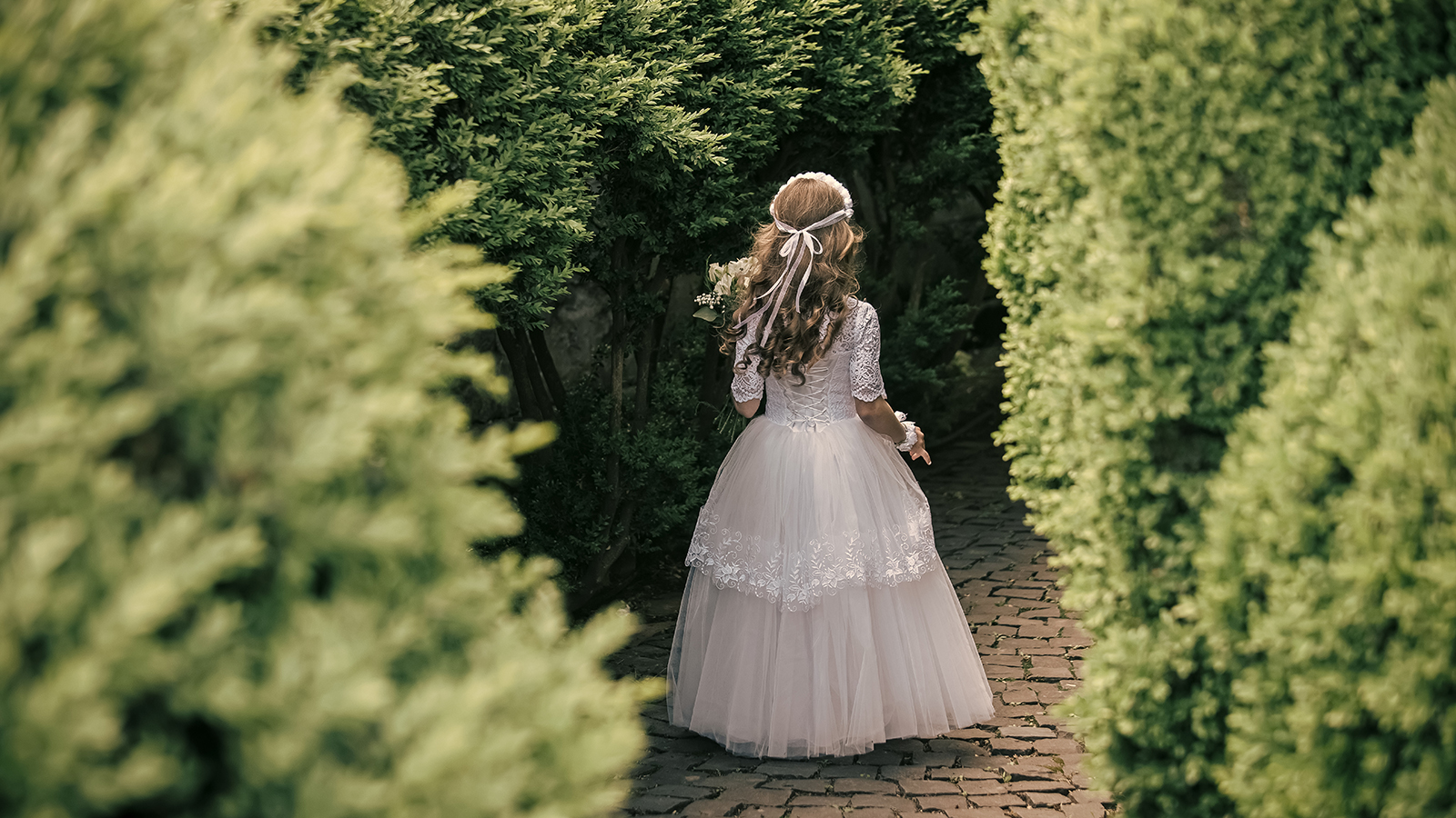 little bridesmaid standing in a green garden with bouquet