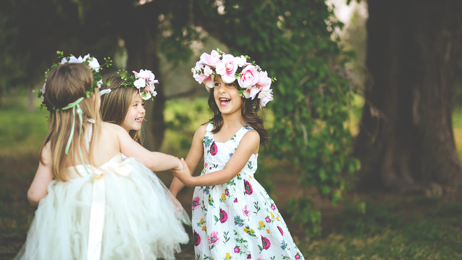 Three adorable girls in dresses hold hands in a circle