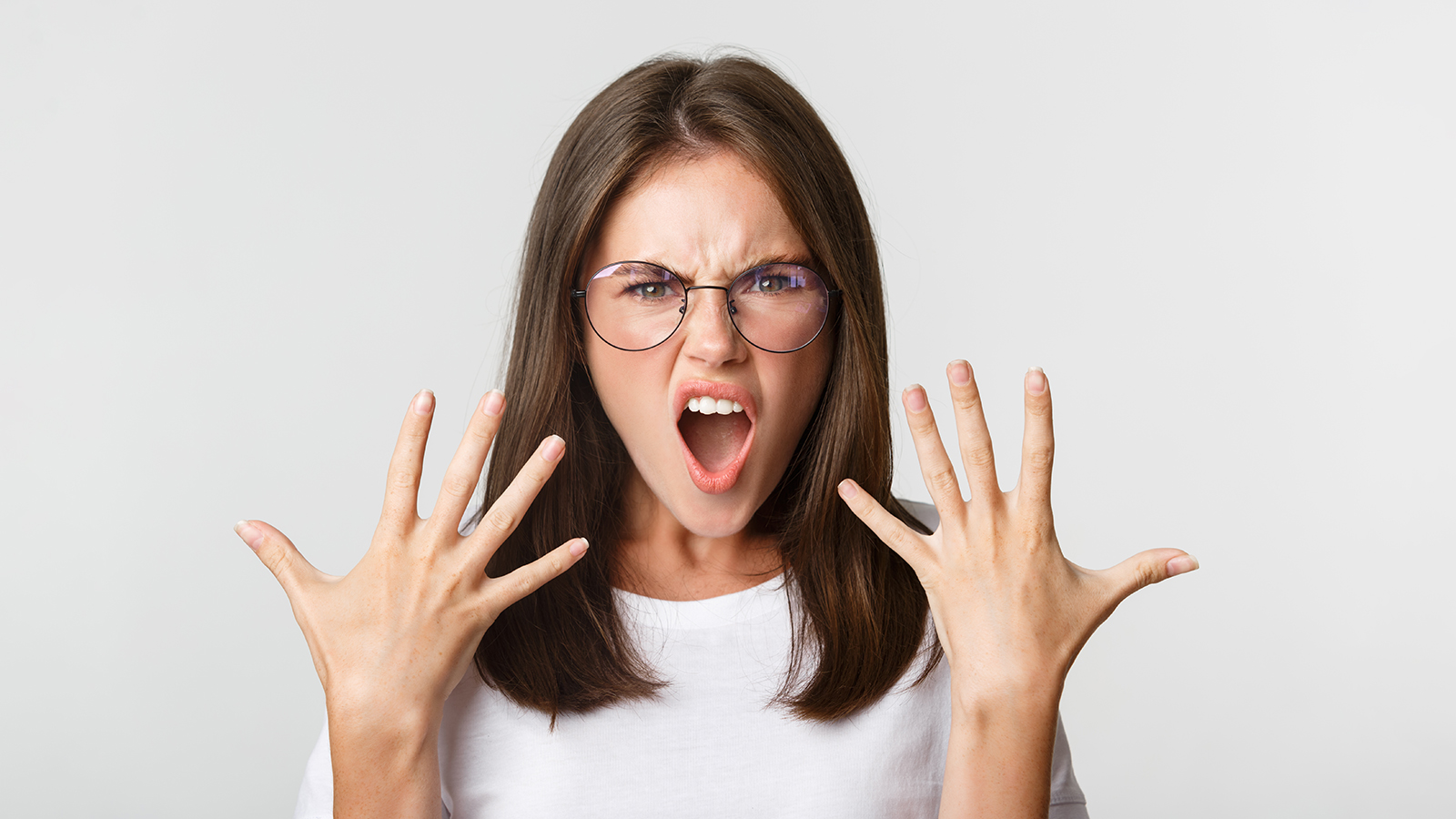 Close-up of angry and furious young woman in glasses arguing, complaining over white background
