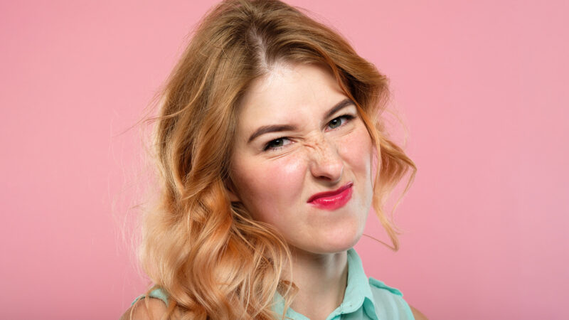 nah, not impressed. unimpressed girl grimacing and wrinkling nose. emotion expression and reaction concept. young beautiful blond girl portrait on pink background.