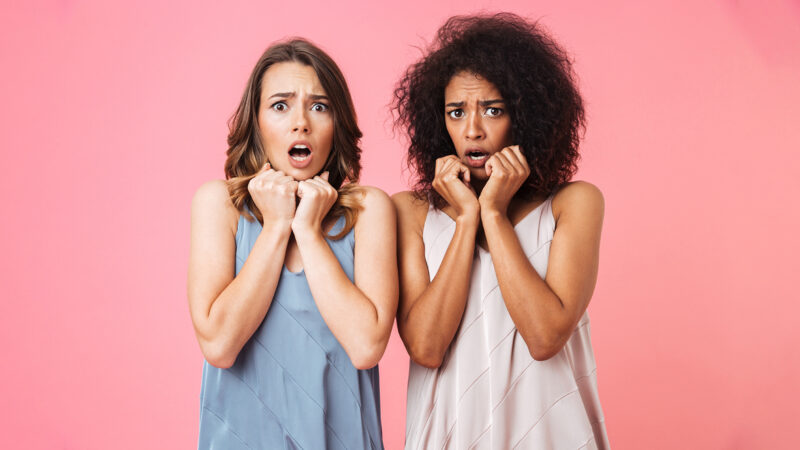 Two scared young girls dressed in summer clothes looking at camera and screaming isolated over pink background