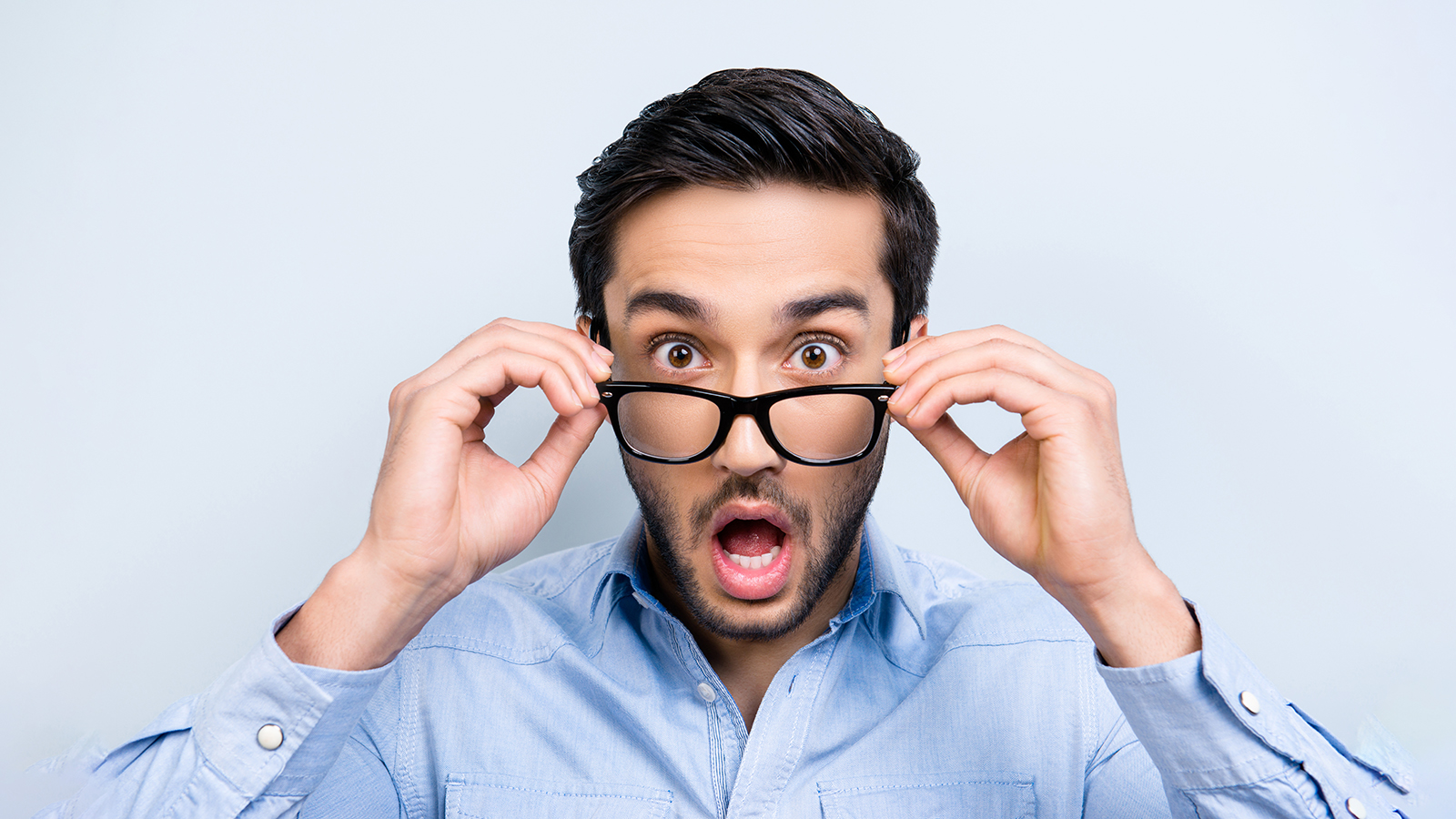 OMG! WTF! Head shot of shocke funny guy with black hair wide open mouth big-eyed looking out glasses on face isolated on grey background