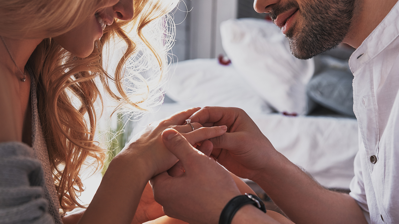 Close-up of young man putting engagement ring on finger of his happy girlfriend