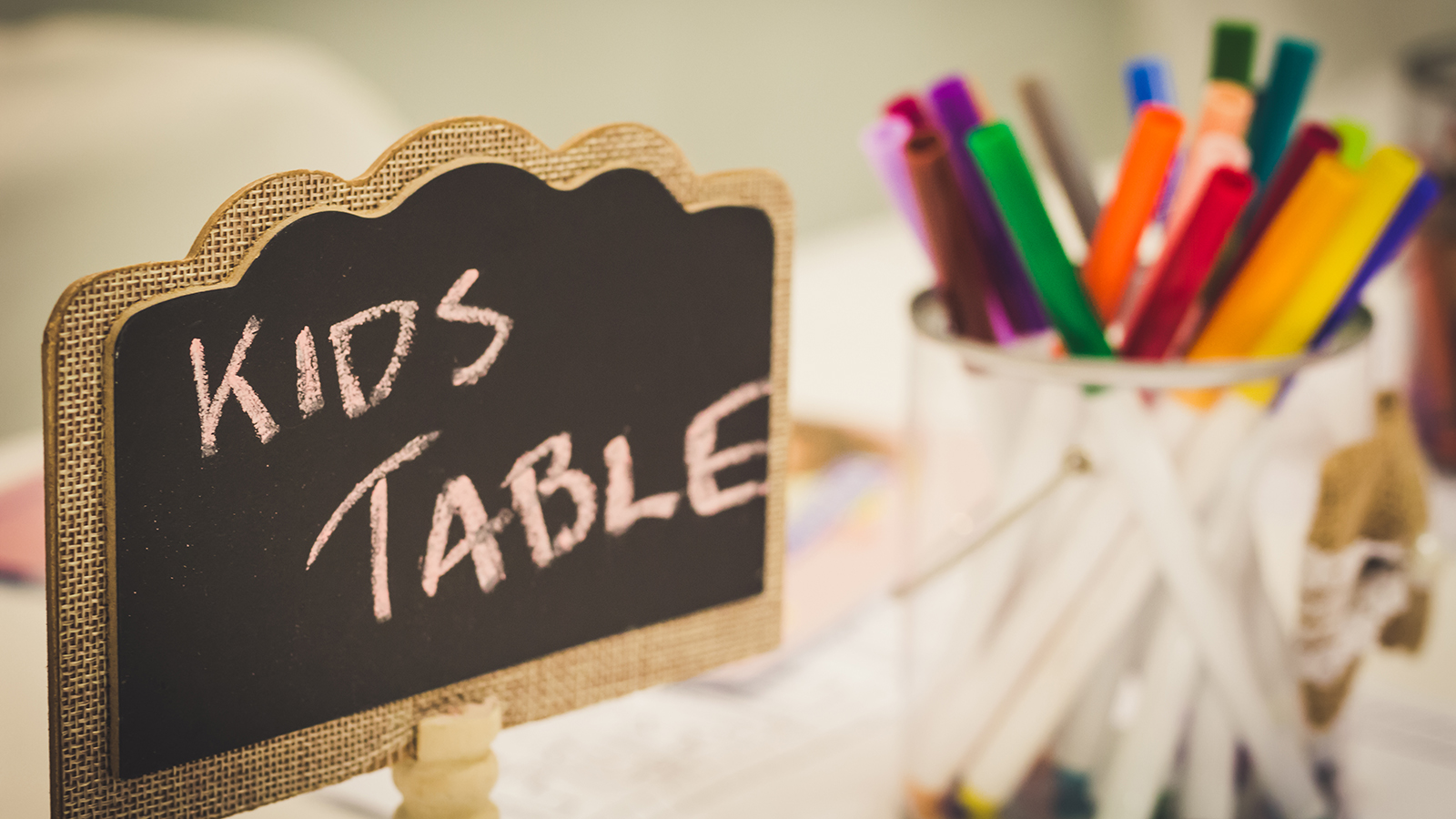 Kids entertainment table at a wedding with colorful markers in a jar and a chalkboard sign