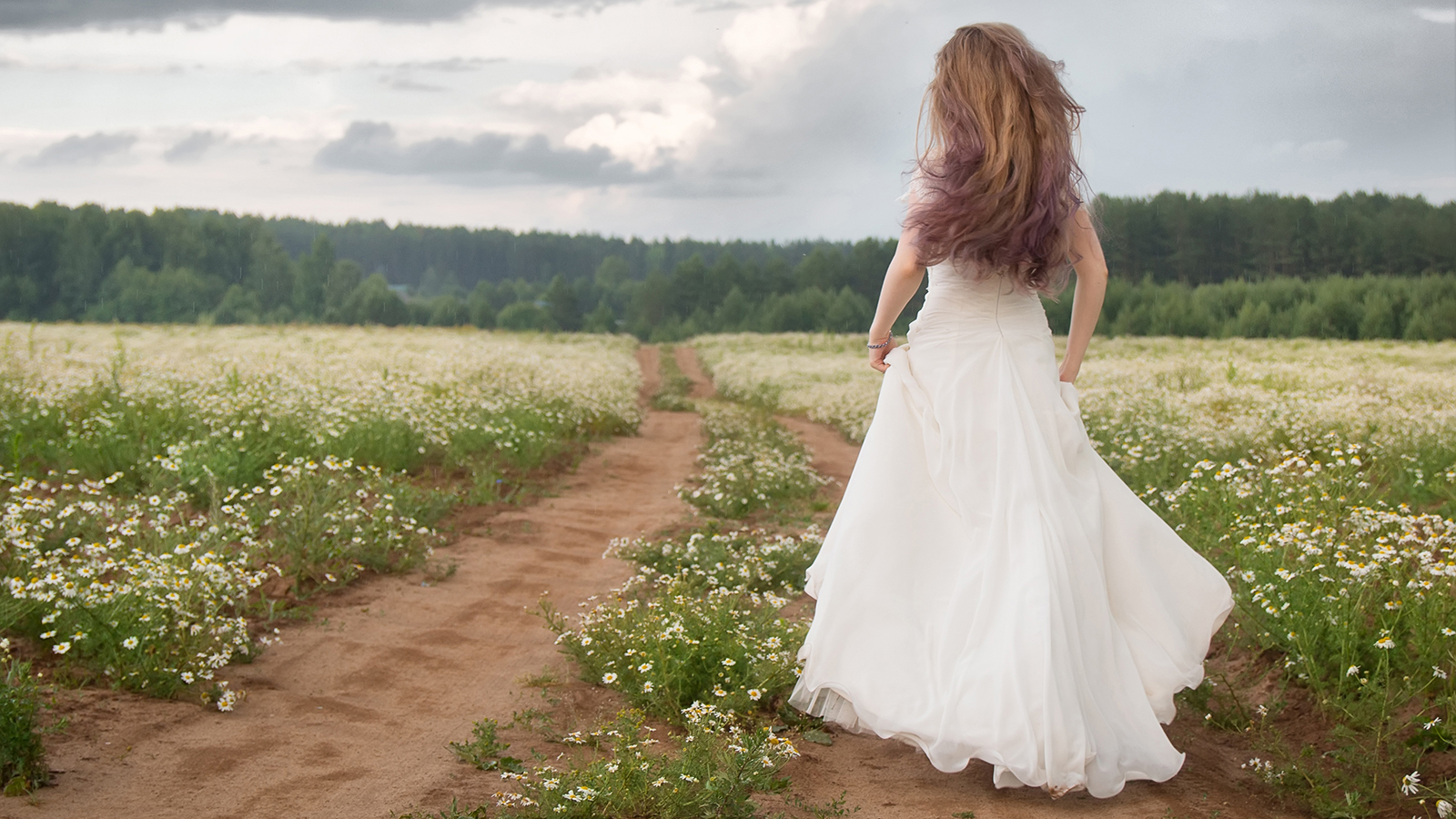 Runaway bride. Woman in a wedding dress runs on flower field.