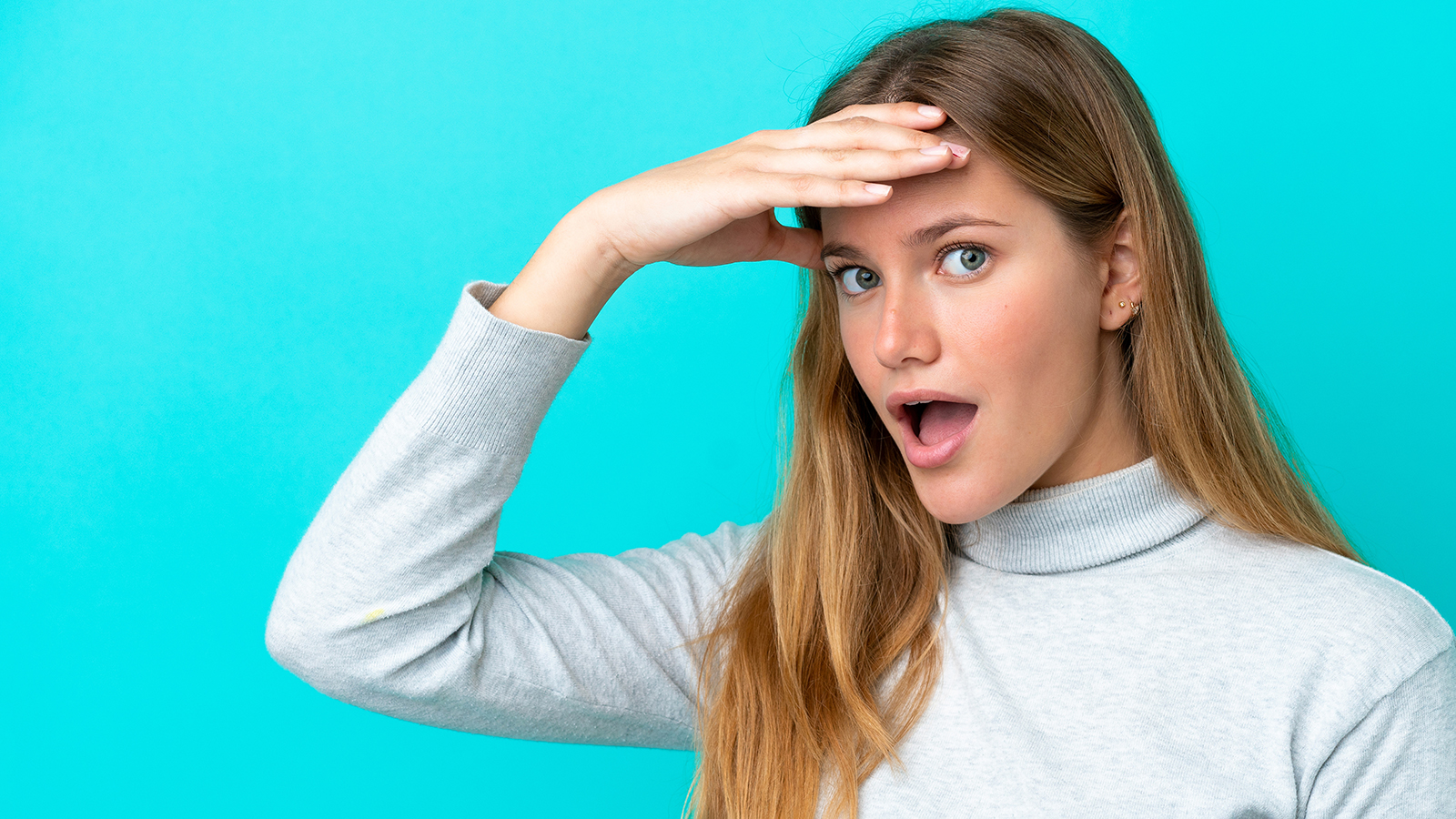 Young blonde woman isolated on blue background doing surprise gesture while looking to the side
