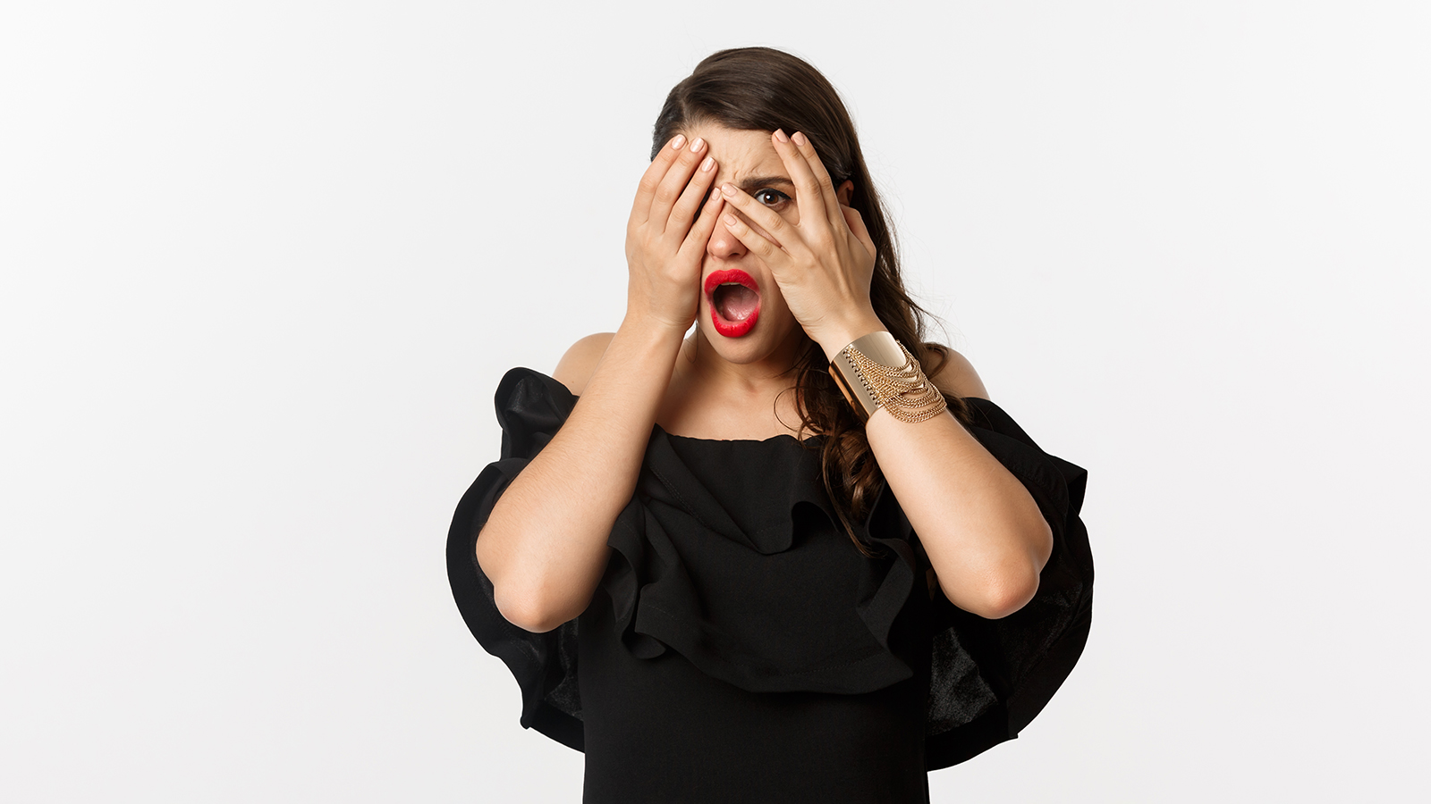 Fashion and beauty. Shocked young woman in black dress covering eyes, peeking through fingers at something embarrassing, cringe, standing over white background