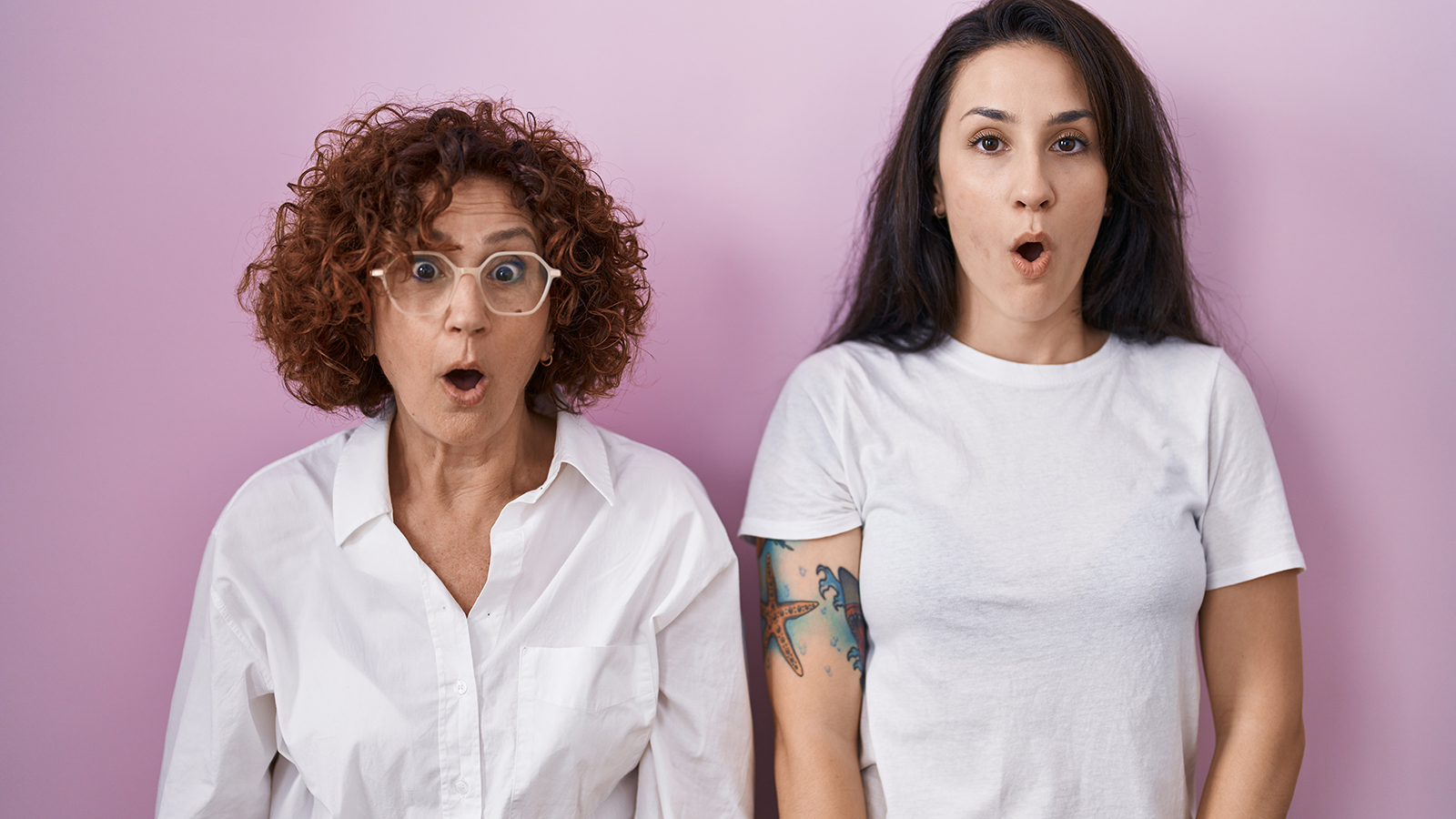 Hispanic mother and daughter wearing casual white t shirt over pink background afraid and shocked with surprise and amazed expression, fear and excited face.
