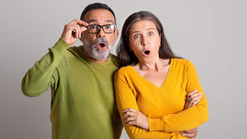 Shocked excited old european man in glasses and lady with open mouth look at camera on gray studio background. Wow, fright, human emotions and facial expression, reaction on good news, ad, offer