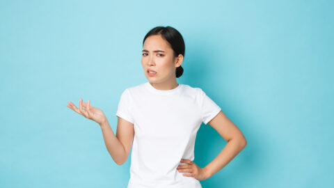 Frustrated and confused asian girl cant understand something, raising hand and looking bothered at camera, arguing with someone, stare questioned and waiting for explanation, blue background