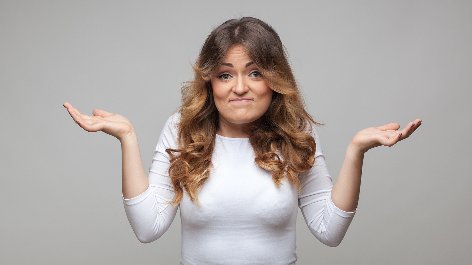 Shrugging woman in doubt doing shrug on grey background
