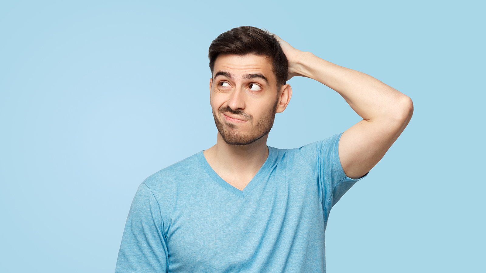 Young doubtful man thinking, scratching head and trying to find solution, isolated on blue background