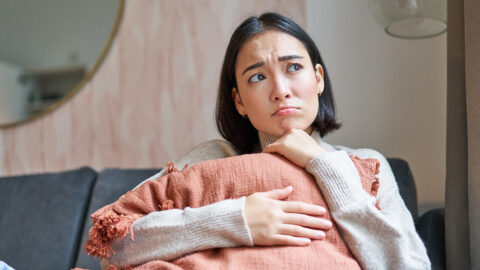 Women and wellbeing concept. Portrait of sad and gloomy asian woman thinking of something unhappy, hugging pillow on sofa and expressing distress.