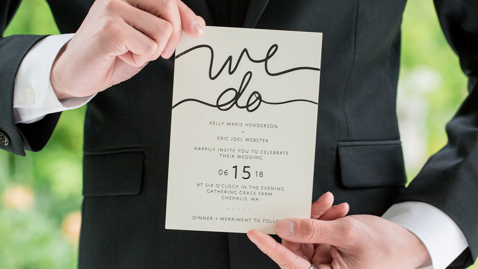 groom in black suit holding wedding invitation