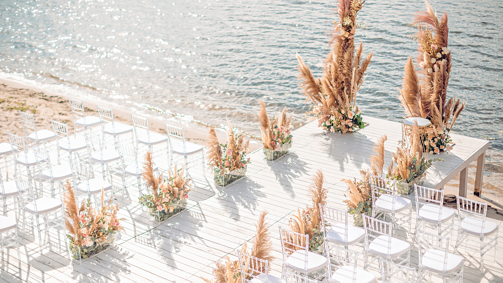 Wedding by the river. Beach wedding venue. Wooden stage with floral decorations arch
