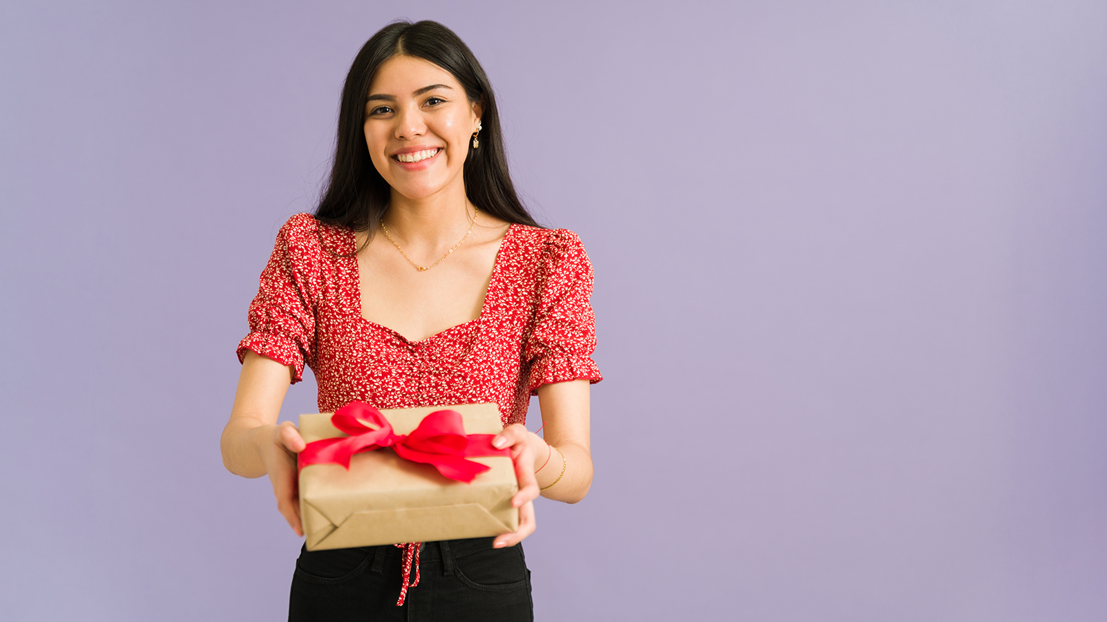 Loving latin young woman giving a beautiful birthday present while smiling against a purple background