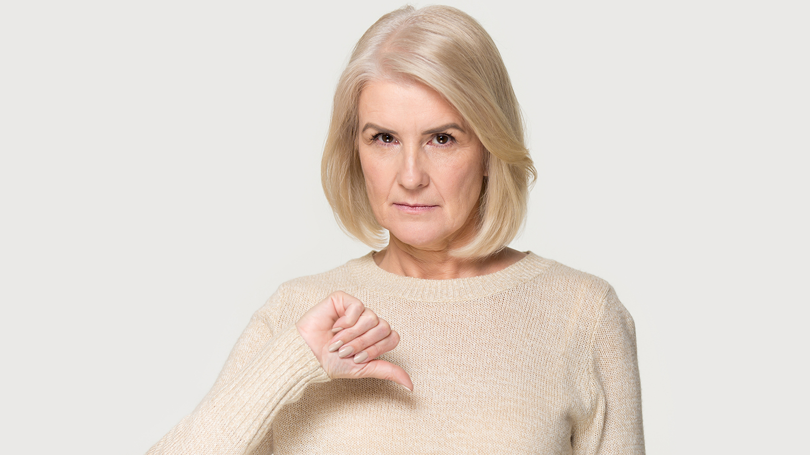 Gloomy dissatisfied mature woman looks at camera show thumbs down isolated on grey studio background, symbol of not approved disapproval negative feedback, disagreement dislike and rejection concept