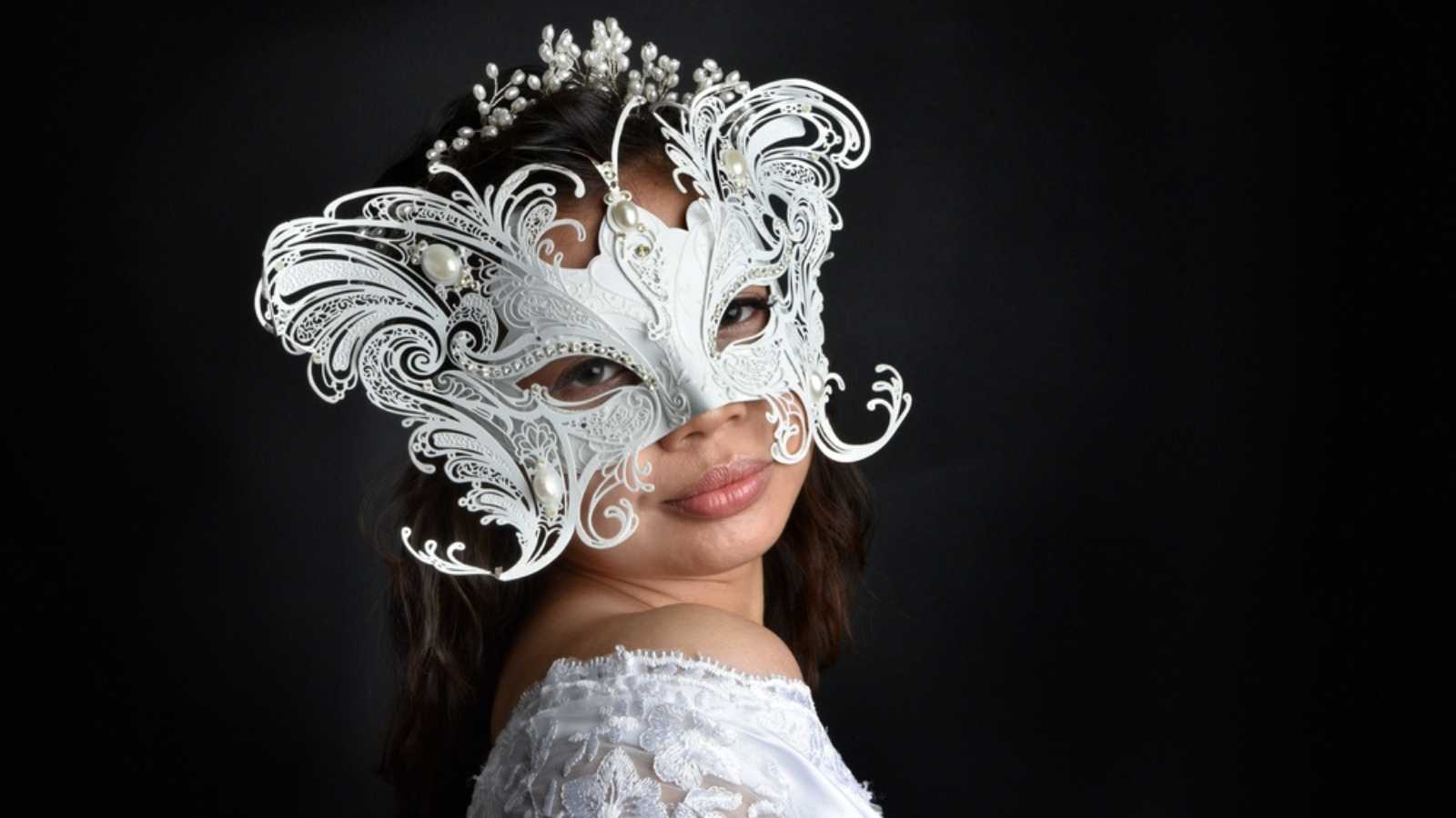 portrait of beautiful woman wearing white lace bridal fantasy gown with butterfly mask. isolated on black studio background.