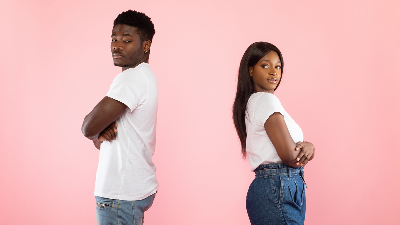 Side view of African American young couple standing separate back to back on pink studio wall. Profile portrait of black man and woman don't talk to each other after family quarrel, crossing arms